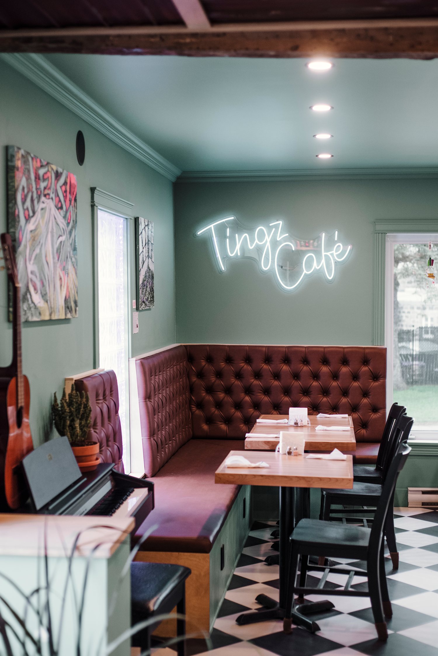 La salle du Tingz Café : banquette capitonnée bordeaux, mur vert sauge et enseigne au néon